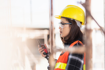 Asian engineer foreman architect worker woman working at building construction site talking with radio, engineering hold radio discuss operate and control worker employee to building construction