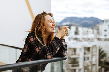 A young, brunette woman dressed in sleepwear enjoys her morning coffee outdoors on the terrace...