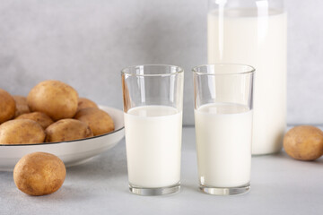 Vegan plant based milk in two transparent glasses. Alternative potato milk and potato tubers on gray table