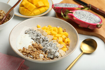 Bowl of granola with pitahaya, mango and yogurt on white marble table
