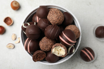 Different delicious chocolate truffles in bowl on light grey table, flat lay