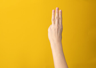 Female hand isolated showing three fingers index, middle and ring on yellow background