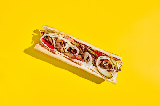 Beef cheesesteak with onion and pickle in minimal style. American fast food in yellow background with shadow. Philly steak sandwich trendy concept. Junk food in colour background.