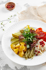 Appetizers from pickled vegetables in white stone background. Authentic food in restaurant menu. Mix from salted tomatoes, cucumber,  pickled pepper, sauerkraut. Assorted from marinated vegetables.