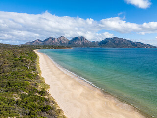 4k high angle aerial drone view of Muirs Beach near Coles Bay with the famous Hazards mountain range in the background, part of Freycinet Peninsula National Park, Tasmania, Australia.	