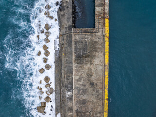 High angle aerial drone bird's eye view of a breakwater sea wall pier structure in Stanley, north-west coast Tasmania, Australia. Stormy sea and big waves splashing on one side of the sea wall.
