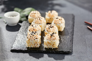 Maki sushi on dark stone table. Sushi roll in seasame and crab topped. Style concept japanesse menu with black background, leaves and hard shadow.