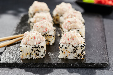 Maki sushi on dark stone table. Sushi roll in seasame and crab topped. Style concept japanesse menu with black background, leaves and hard shadow.