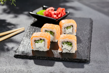 Maki sushi on dark stone table. Philadelphia maki with salmon. Sushi roll with cheese, cucumber inside, salmon outside. Style concept japanese menu with black background, leaves and hard shadow.