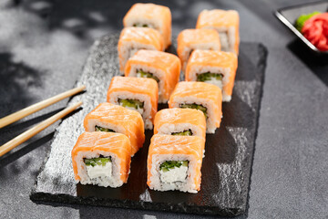 Maki sushi on dark stone table. Philadelphia maki with salmon. Sushi roll with cheese, cucumber inside, salmon outside. Style concept japanese menu with black background, leaves and hard shadow.