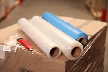 Rolls of different stretch wraps and utility knife on boxes in warehouse