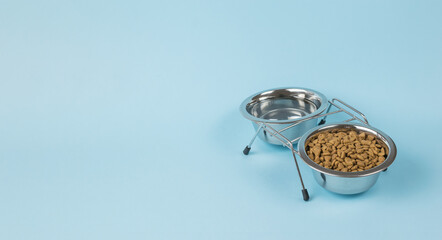 Two bowls filled with dry food and water on a blue background. Place for text.