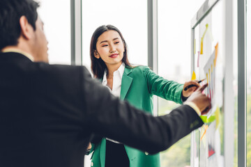 Casual creative happy two smile asian business people plan strategy analysis and brainstorm putting post it sticker note to share idea for startup project on glass board at modern office