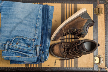 old shoes and  stack of blue jeans  lie on a vintage suitcase. The concept of travel and comfortable equipment
