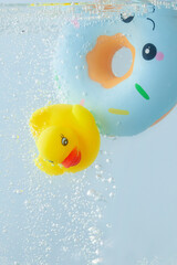 Yellow rubber toy duck and lifebuoy in a blue pool with bubbles. Summer concept.