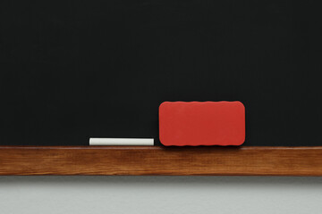 Clean blackboard with chalk and duster hanging on grey wall