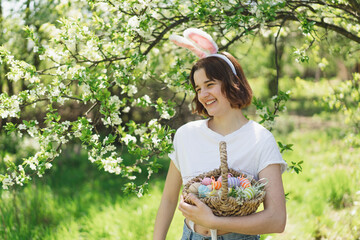 Easter egg hunt in spring garden. Funny teen girl with eggs basket and bunny ears on Easter egg...