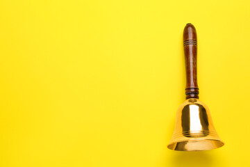 Golden school bell with wooden handle on yellow background, top view. Space for text - obrazy, fototapety, plakaty