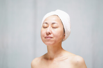 頭にタオルを巻いて目を閉じる素顔の中年女性　