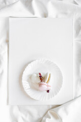 A pink heart-shaped cake lies on a white plate on a light background. Light macaroons on a white canvas. Valentine's Day background