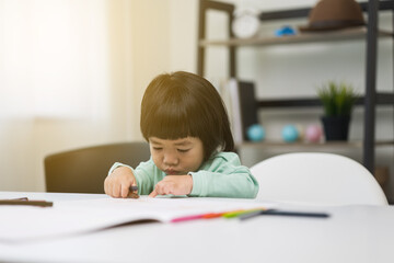 Naklejka premium Happy asian boy painting with crayon and colored pencil in living room at home. Little boy doing homework Practice the skills of drawing and painting.