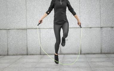 Fitness woman rope skipping against city wall - obrazy, fototapety, plakaty