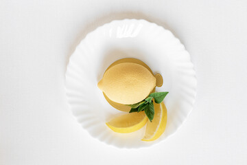 Mousse yellow cake in the form of a lemon with a green mint leaf and real lemon slices on a white...