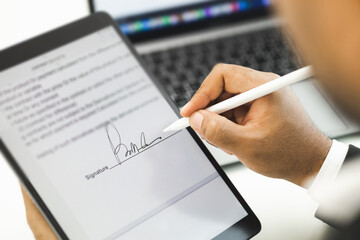 Fototapeta na wymiar Close up businessman hand electronic Signature on Tablet by Stylus. Write business agreement of contract. Man signing contract on tablet. Business and technology concept.