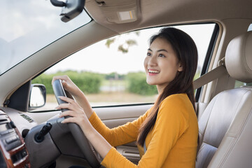 Young beautiful asian women getting new car. she very happy and excited Look the rearview mirror while reversing the car. Smiling female driving vehicle on the road on a bright day