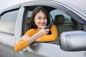 Young beautiful asian women getting new car. she very happy and excited looking outside window in hand holding car key. Smiling female driving vehicle on the road on a bright day