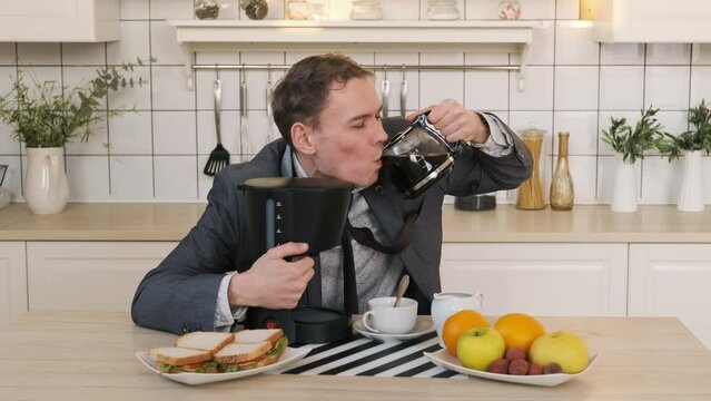 Sleepy Businessman Hugs Coffee Machine and Drinking Coffee while Sitting at Table in the Kitchen. Business, Lifestyle, Overworking, Caffeine Addiction Concept