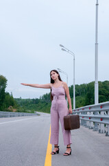 Naklejka premium A girl with a suitcase is voting on an empty road waiting for a car
