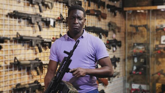 African-american man choosing machine gun in air weapon shop.