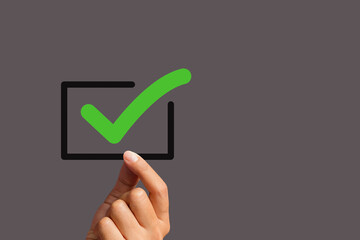 Hand holding a green check mark symbol with a black border against a gray background.