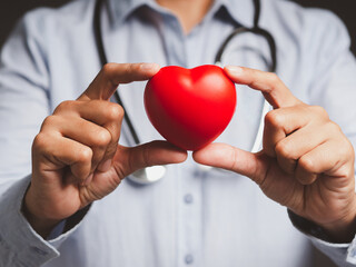 Hand of a doctor holding a red heart shape while standing in the hospital or clinic.