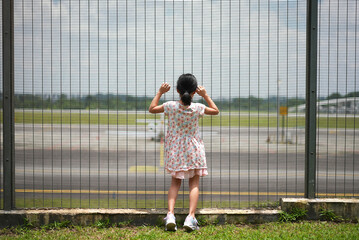 Little asian child looking at airport behind fence longing for travel