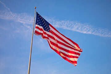 Single, large, isolated US flag flying high on a flagpole against a clear blue sky