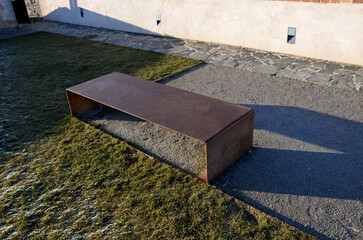 a bench of one piece of sheet metal in a regular garden with a stone walkway of gray flat slate....