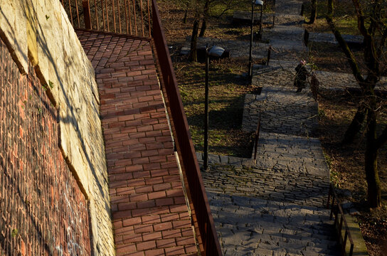 road along the baroque bastion. modern railing made of corten sheet metal. The sidewalk is paved with burnt bricks. the high wall of the walls is sloping to reflect artillery projectiles upwards