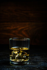 Glass chilled whiskey with ice cubes on wooden background in cellar.