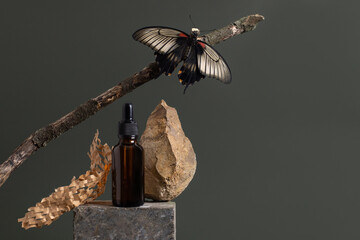 Brown glass bottle of cosmetic product or oil on stone with levy butterfly in green background....