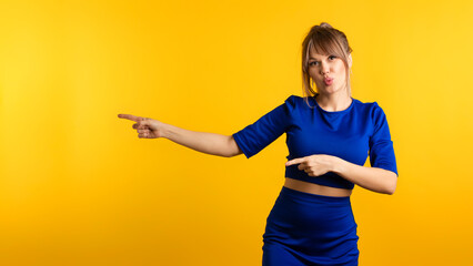 Funny Girl pointing index fingers aside on the left and looking at camera on yellow background....