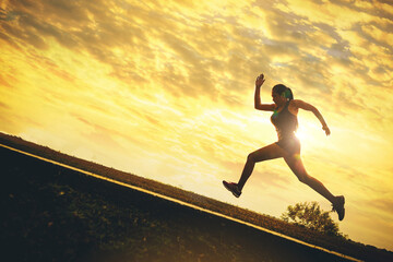 Fototapeta na wymiar Silhouette of young woman running sprinting on road. Fit runner fitness runner during outdoor workout with sunset background. 