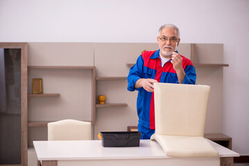 Old male carpenter repairing chair indoors