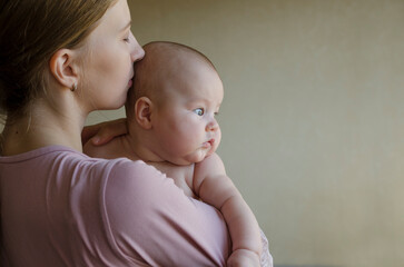 A young mother holds a newborn baby, kisses the head at home in a bedroom. Motherhood, seven, happiness, mother's care, love concept