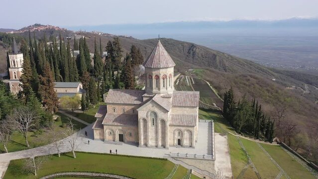 Scenic spring aerial view of monastic complex of Bodbe nunnery on hillside among tall Cypress trees with Church of St. Nino on sunny day, Sighnaghi, Georgia