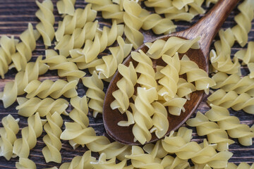 Pasta in the shape of a spiral in a wooden spoon on a dark wooden background
