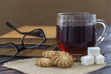 A cup of tea, cookies, three pieces of sugar, books and glasses.