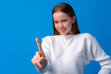 Cheerful teenage girl pointing finger at camera on blue background