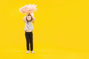 Gift for mom. Women's day. Mothers day. The girl holds a huge flower above her head on a yellow...
